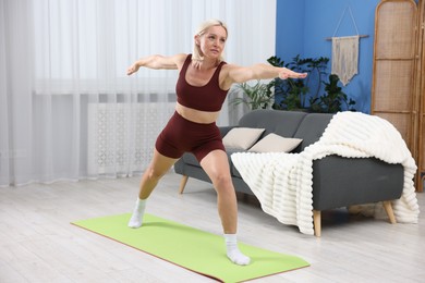 Photo of Mature woman in sportswear stretching on mat at home
