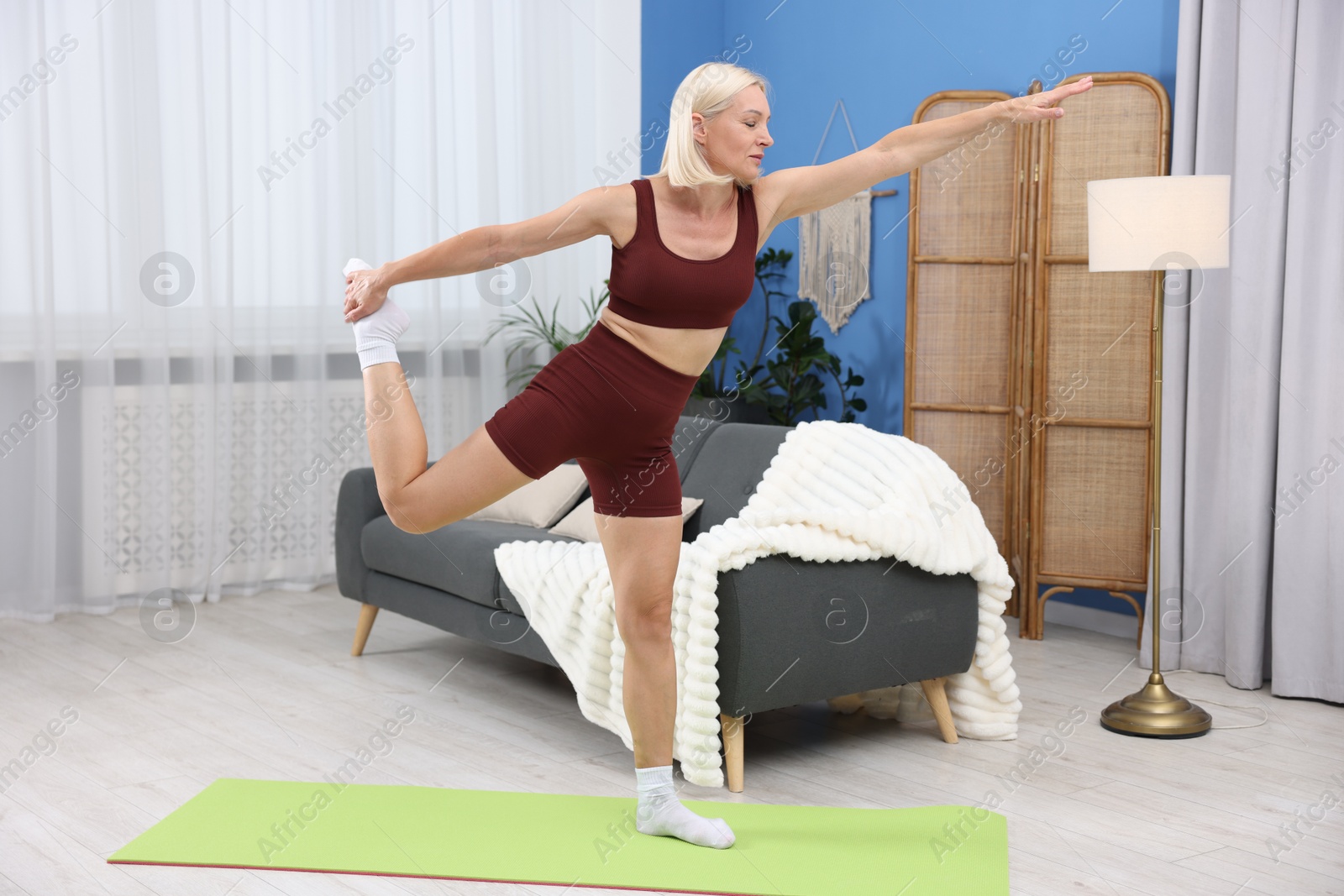 Photo of Mature woman in sportswear stretching on mat at home