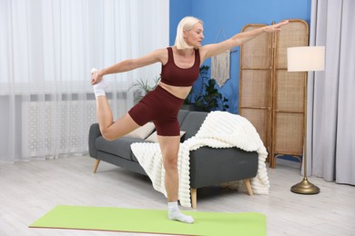 Photo of Mature woman in sportswear stretching on mat at home