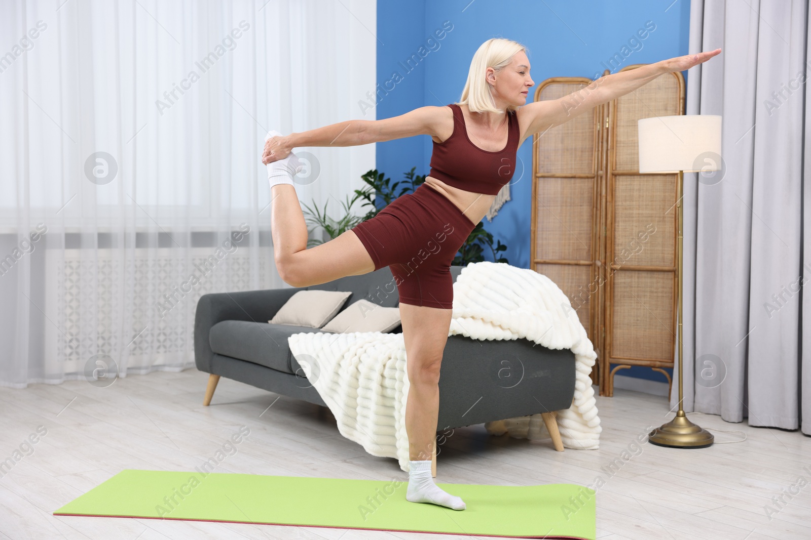 Photo of Mature woman in sportswear stretching on mat at home