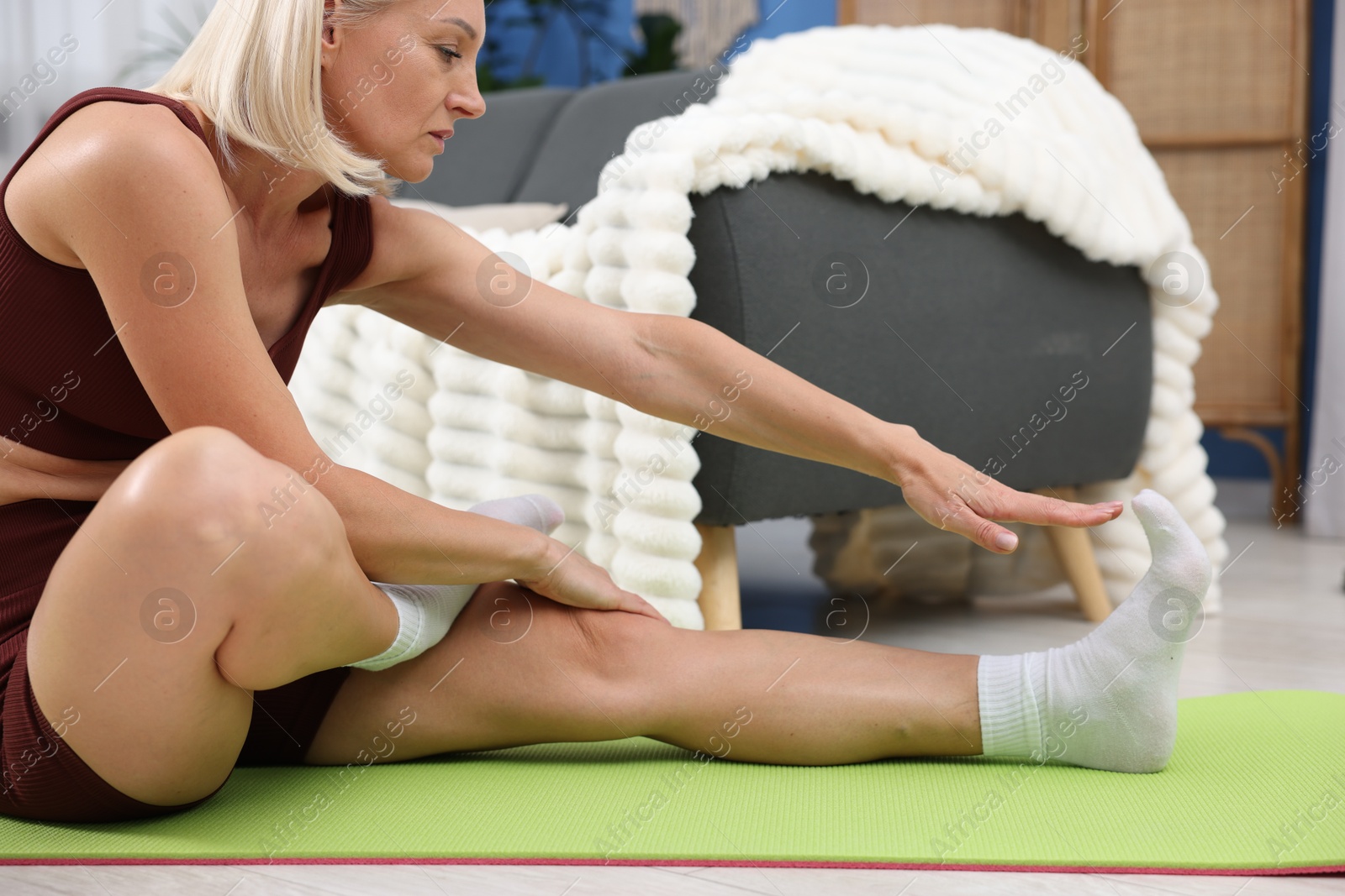 Photo of Mature woman in sportswear stretching on mat at home