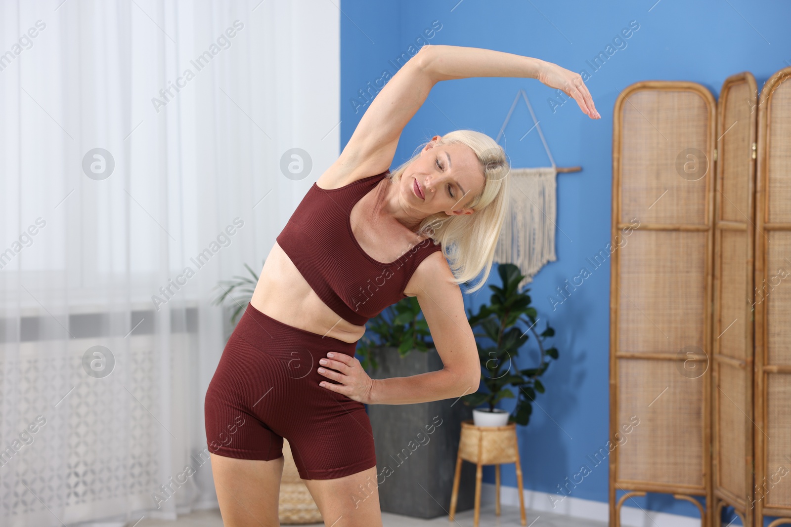 Photo of Mature woman in sportswear stretching at home