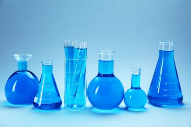 Photo of Different laboratory glassware with bright liquid on light blue gradient background