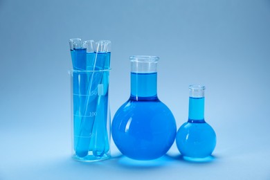 Photo of Different laboratory glassware with bright liquid on light blue gradient background