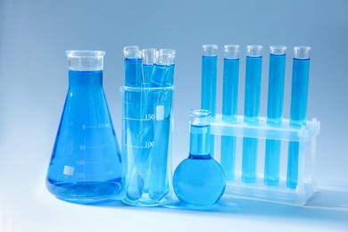 Photo of Different laboratory glassware with bright liquid on light blue gradient background