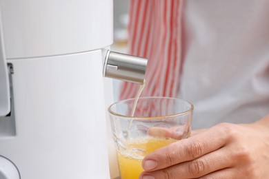 Photo of Woman making fresh orange juice with modern juicer indoors, closeup