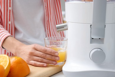 Photo of Woman making fresh orange juice with modern juicer at table indoors, closeup