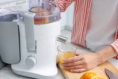 Photo of Woman making fresh orange juice with modern juicer at white marble table indoors, closeup