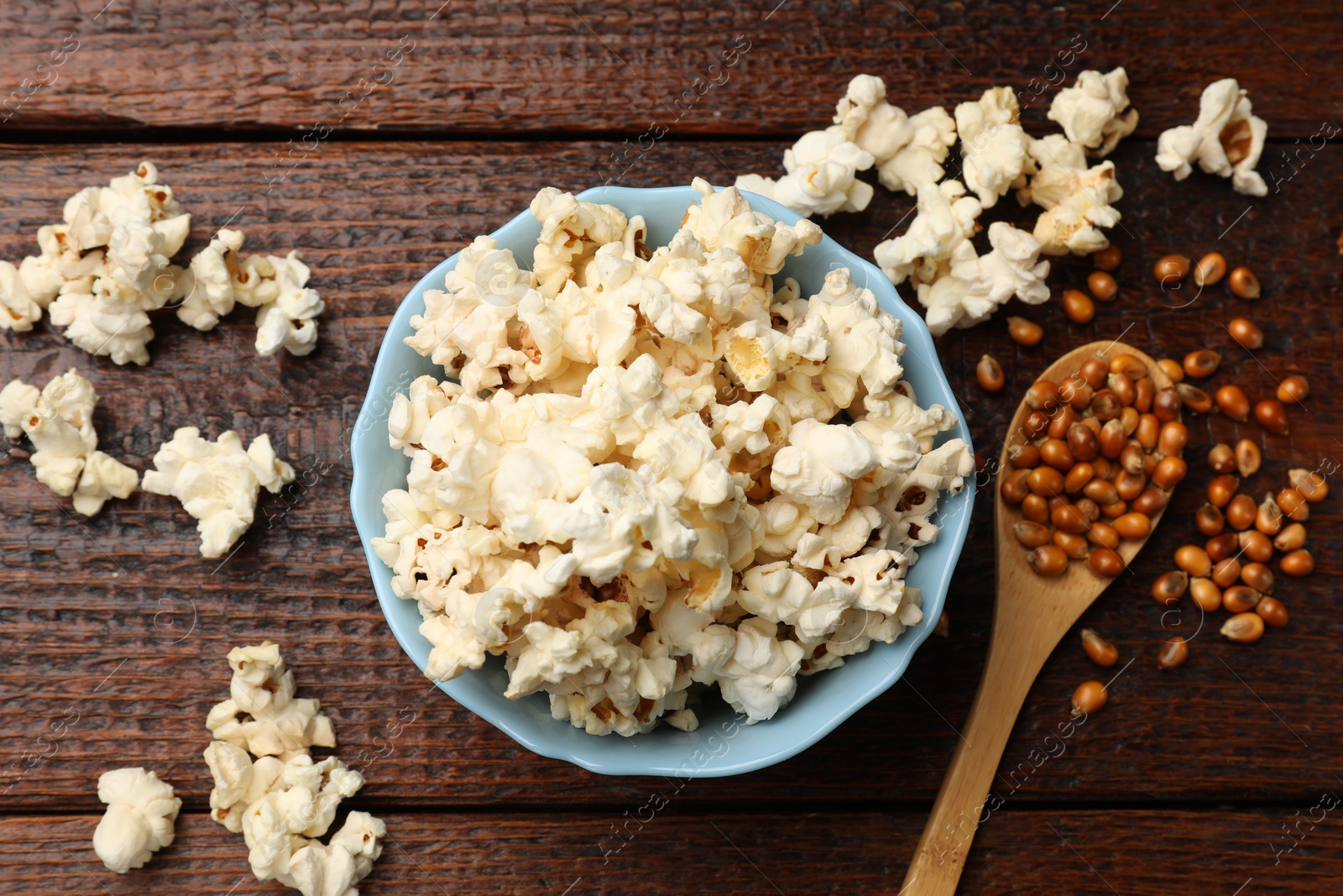 Photo of Tasty popcorn and corn kernels on wooden table, flat lay