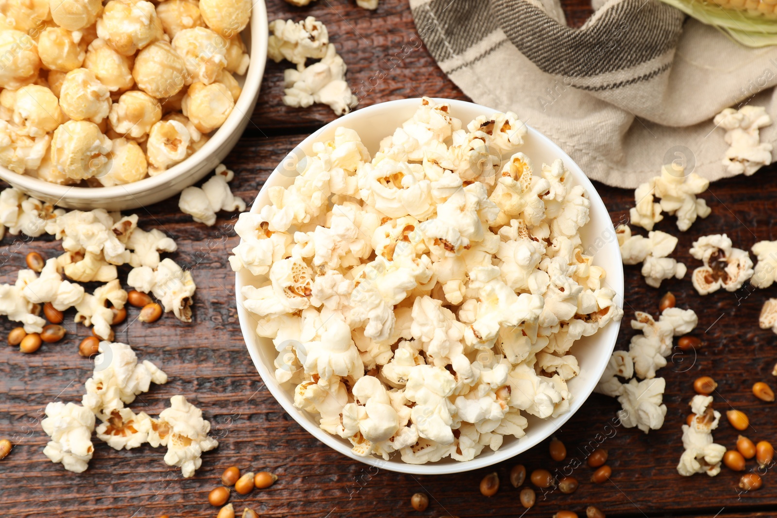 Photo of Tasty popcorn and corn kernels on wooden table, flat lay