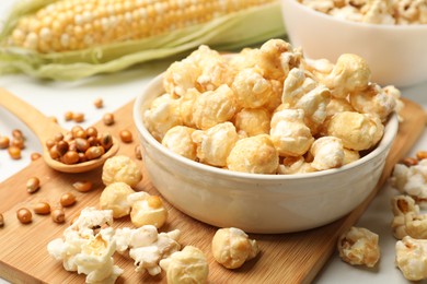 Photo of Tasty popcorn, corncob and corn kernels on white table, closeup