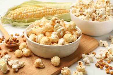 Photo of Tasty popcorn, corncob and corn kernels on white table, closeup
