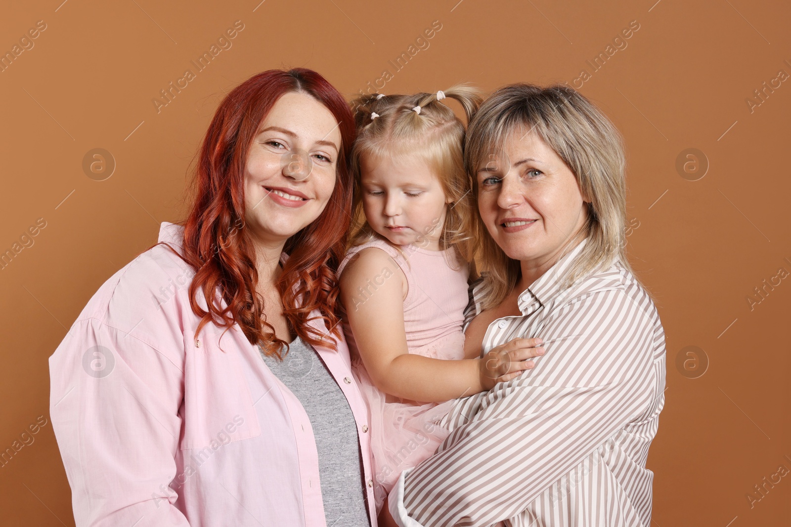 Pregnant woman, her mother and daughter on brown background Photo of Pregnant woman, her mother and daughter on brown background