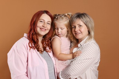 Photo of Pregnant woman, her mother and daughter on brown background