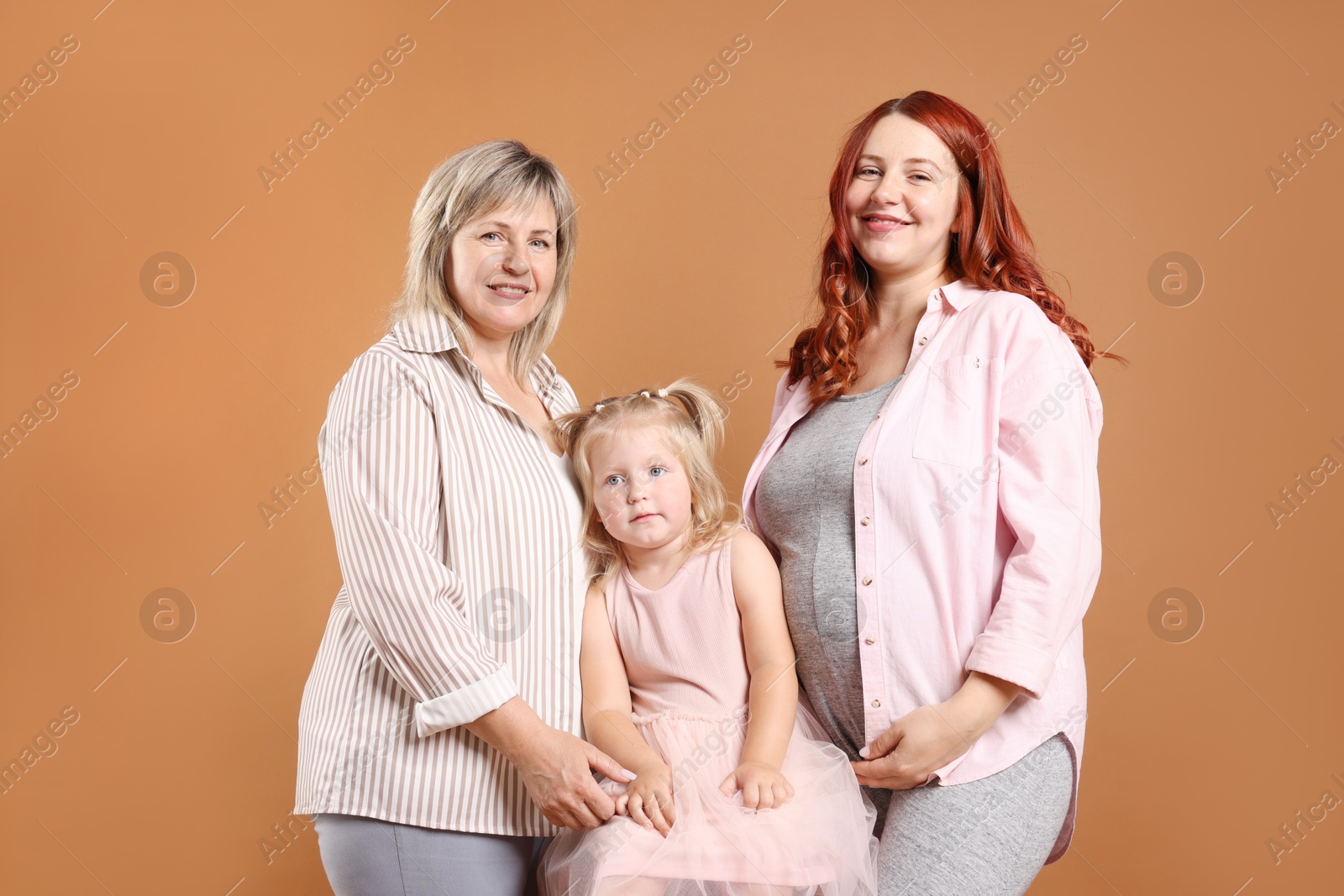 Pregnant woman, her mother and daughter on brown background Photo of Pregnant woman, her mother and daughter on brown background