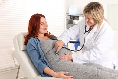 Photo of Pregnancy checkup. Doctor with stethoscope listening baby's heartbeat in patient's tummy indoors