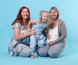 Photo of Pregnant woman, her mother and daughter on light blue background