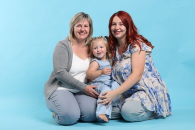 Photo of Pregnant woman, her mother and daughter on light blue background