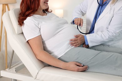 Photo of Pregnancy checkup. Doctor with stethoscope listening baby's heartbeat in patient's tummy indoors, closeup