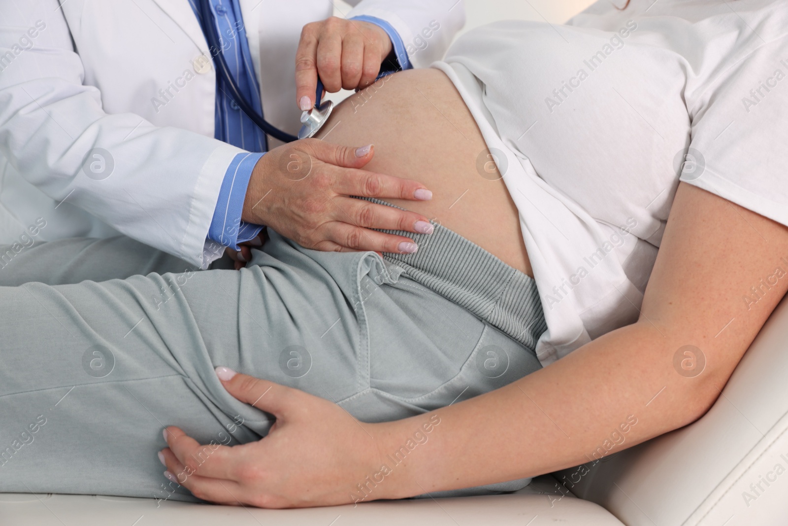 Photo of Pregnancy checkup. Doctor with stethoscope listening baby's heartbeat in patient's tummy indoors, closeup