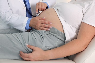 Photo of Pregnancy checkup. Doctor with stethoscope listening baby's heartbeat in patient's tummy indoors, closeup
