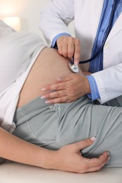 Photo of Pregnancy checkup. Doctor with stethoscope listening baby's heartbeat in patient's tummy indoors, closeup