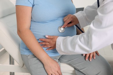 Photo of Pregnancy checkup. Doctor with stethoscope listening baby's heartbeat in patient's tummy indoors, closeup