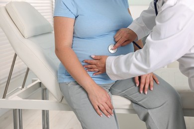 Photo of Pregnancy checkup. Doctor with stethoscope listening baby's heartbeat in patient's tummy indoors, closeup