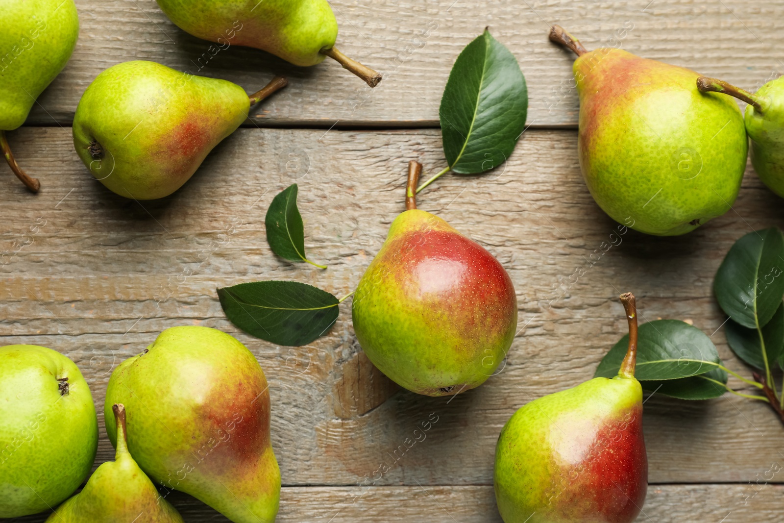 Photo of Fresh ripe pears and green leaves on wooden table, flat lay