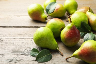 Photo of Fresh ripe pears and green leaves on wooden table, closeup. Space for text