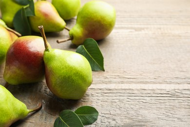 Photo of Fresh ripe pears and green leaves on wooden table, closeup. Space for text