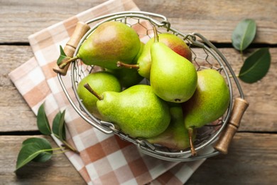 Photo of Fresh ripe pears in metal basket and green leaves on wooden table, flat lay