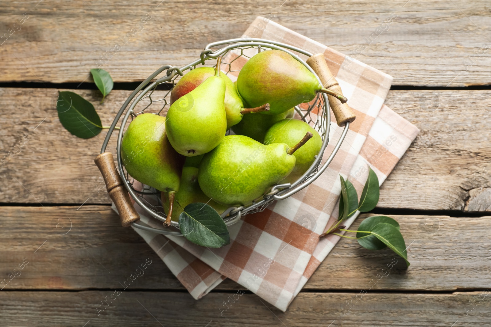 Photo of Fresh ripe pears in metal basket and green leaves on wooden table, flat lay