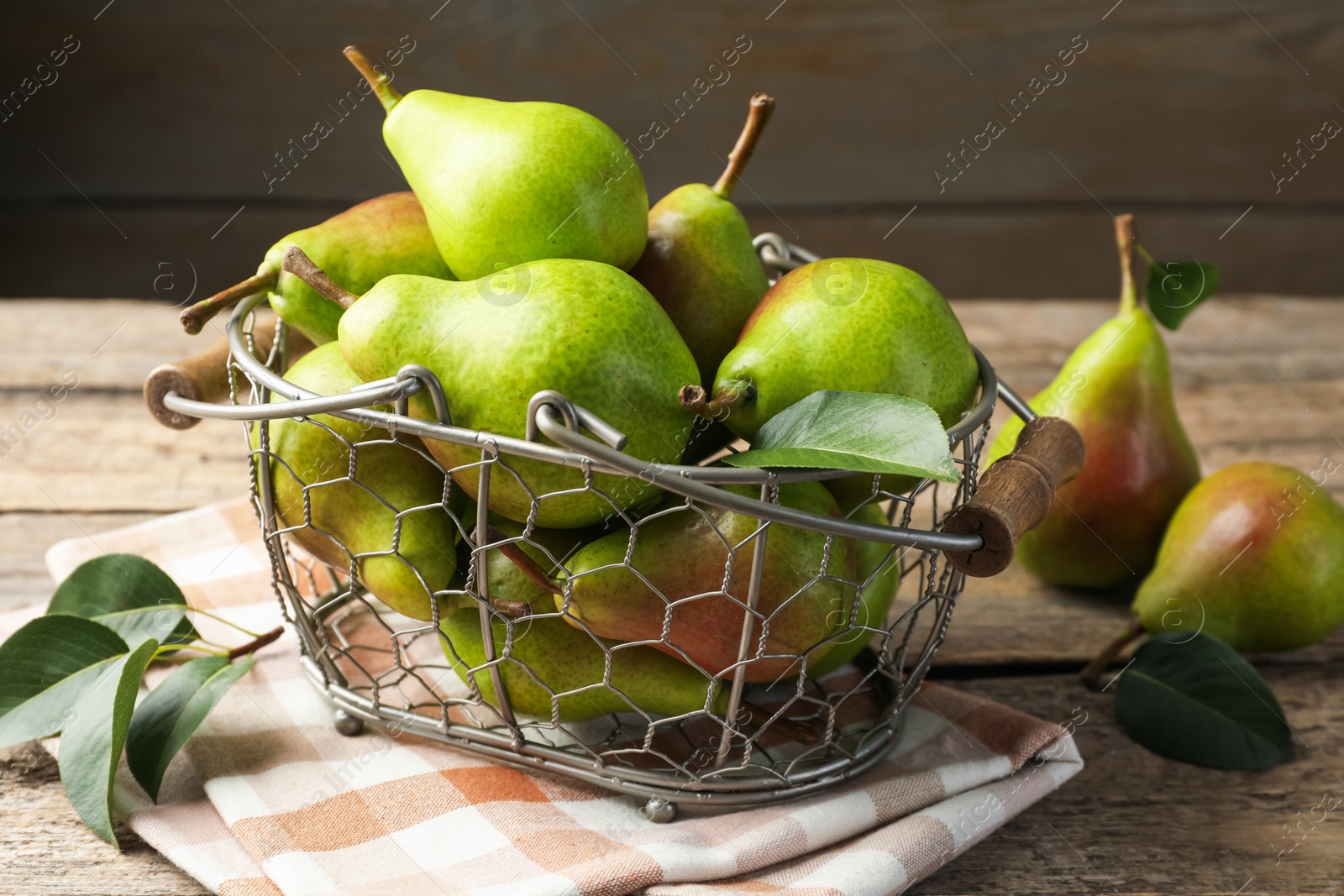 Photo of Fresh ripe pears in metal basket and green leaves on wooden table, closeup