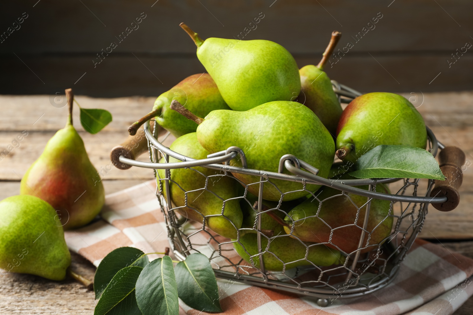 Photo of Fresh ripe pears in metal basket and green leaves on wooden table, closeup