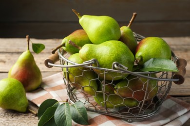 Photo of Fresh ripe pears in metal basket and green leaves on wooden table, closeup