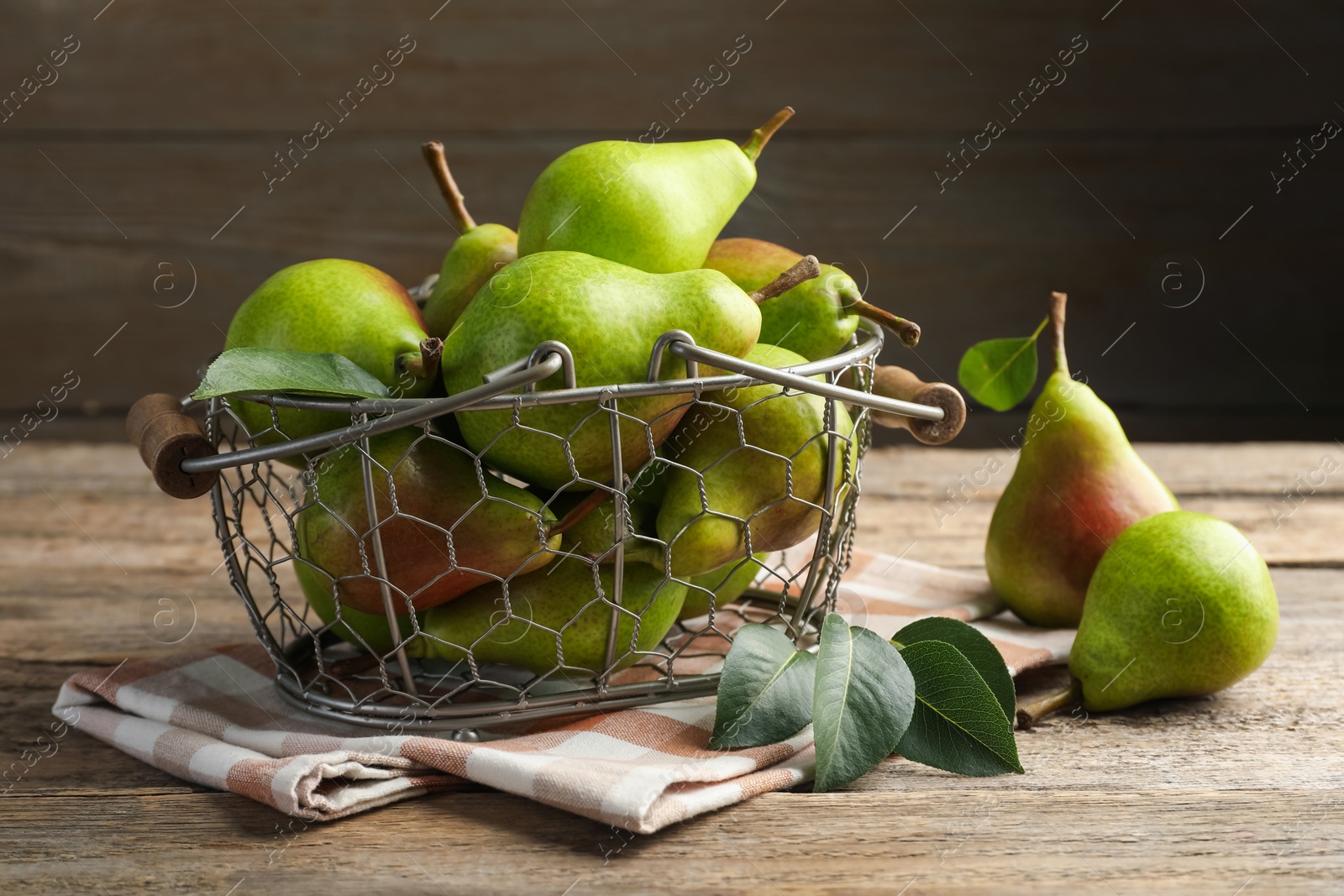 Photo of Fresh ripe pears in metal basket and green leaves on wooden table