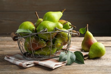 Photo of Fresh ripe pears in metal basket and green leaves on wooden table