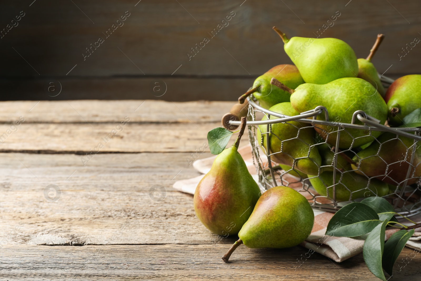 Photo of Fresh ripe pears in metal basket and green leaves on wooden table, closeup. Space for text
