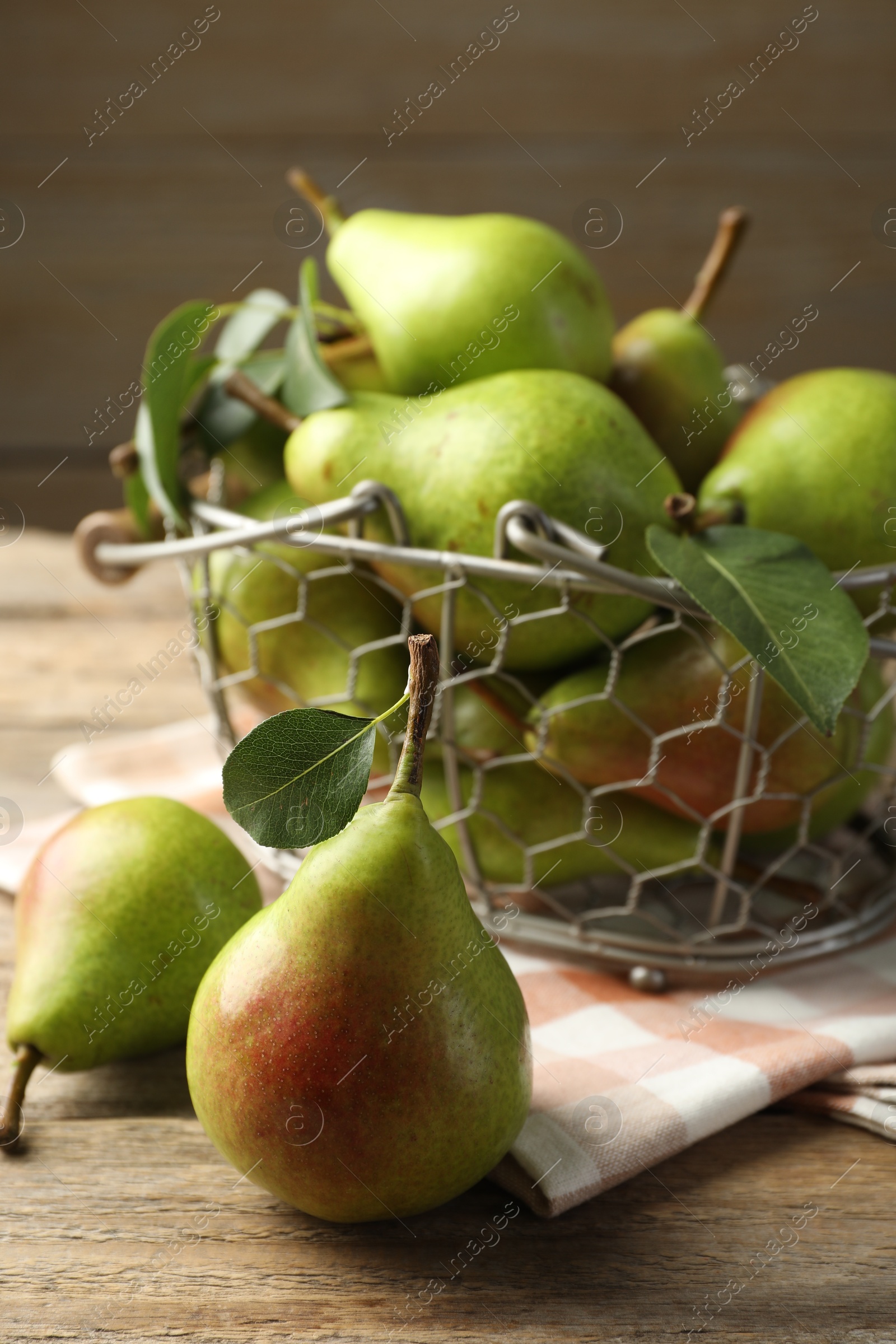 Photo of Fresh ripe pears in metal basket and green leaves on wooden table, closeup