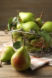 Photo of Fresh ripe pears in metal basket and green leaves on wooden table, closeup