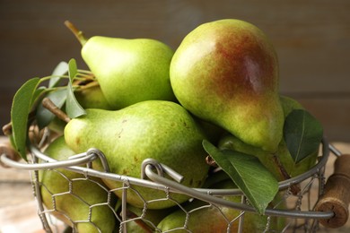 Photo of Fresh ripe pears and green leaves in metal basket on table, closeup