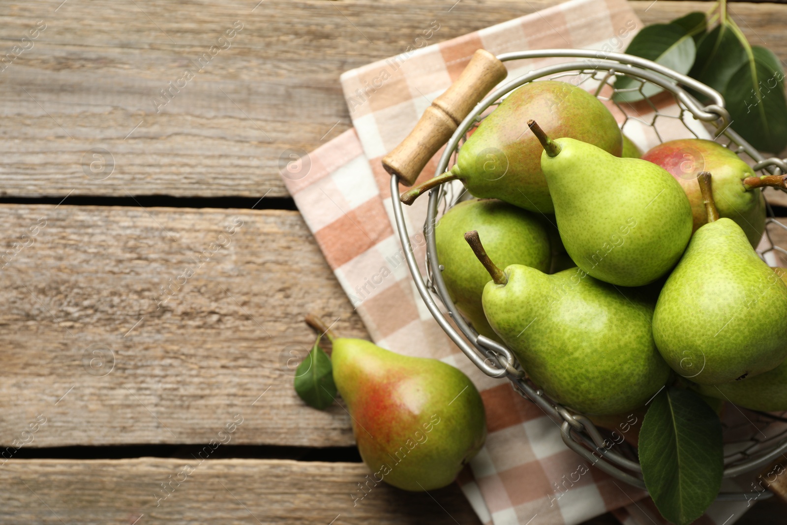 Photo of Fresh ripe pears in metal basket and green leaves on wooden table, flat lay. Space for text