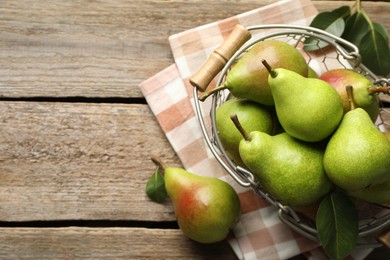 Photo of Fresh ripe pears in metal basket and green leaves on wooden table, flat lay. Space for text