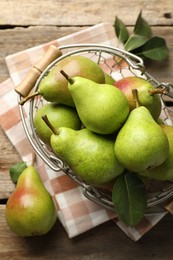 Photo of Fresh ripe pears in metal basket and green leaves on wooden table, flat lay
