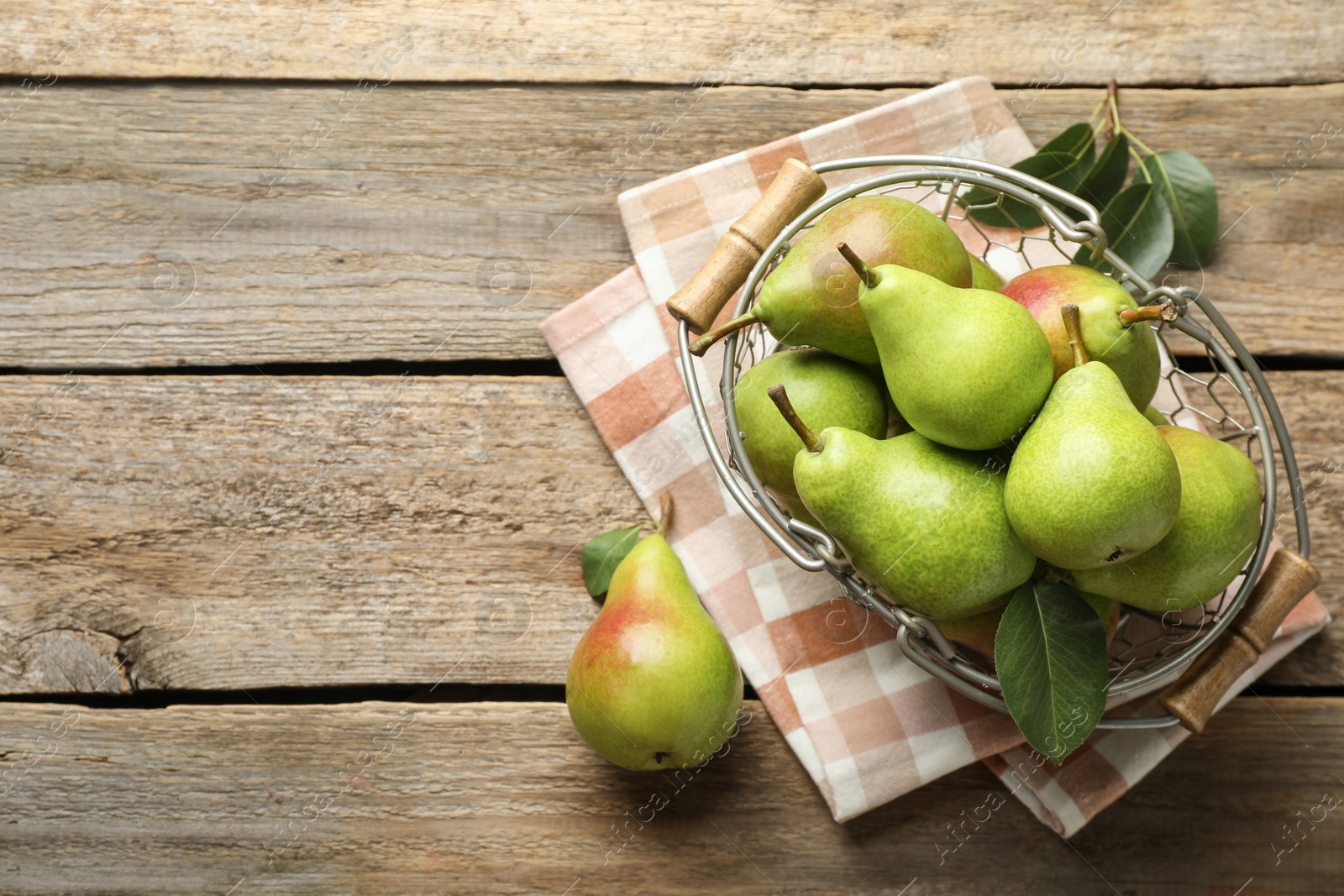 Photo of Fresh ripe pears in metal basket and green leaves on wooden table, flat lay. Space for text