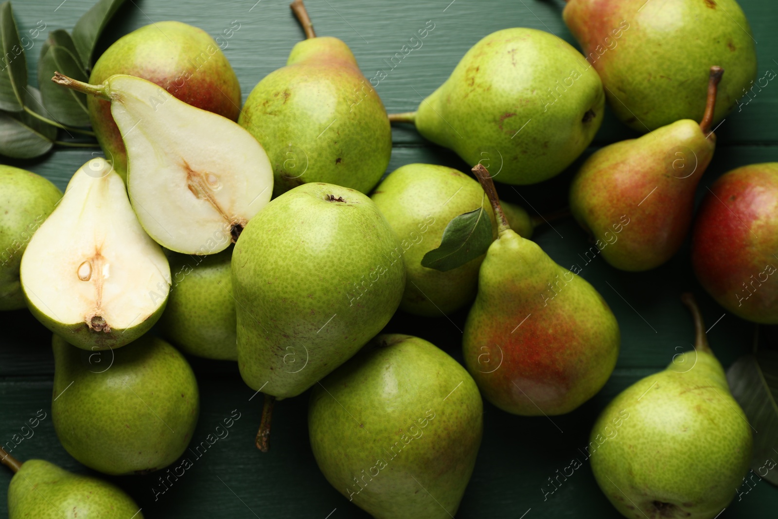 Photo of Fresh ripe pears and leaves on green wooden table, flat lay