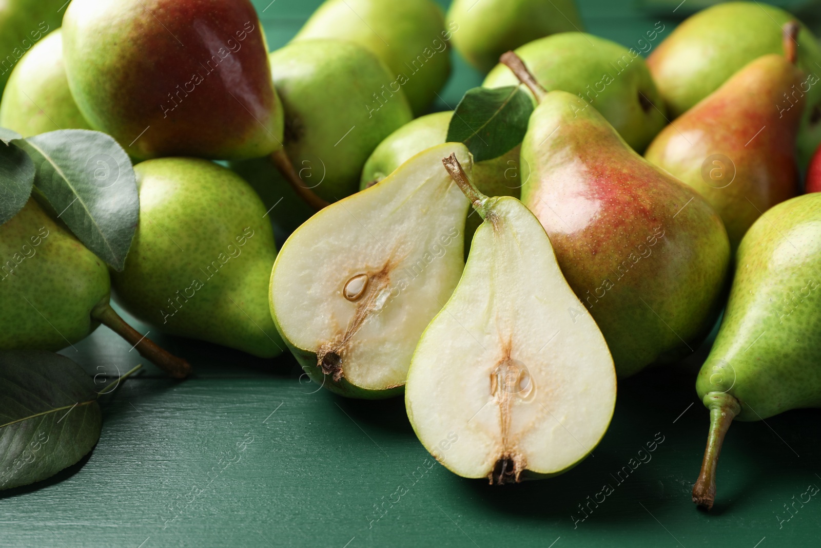 Photo of Fresh ripe pears and leaves on green wooden table, closeup