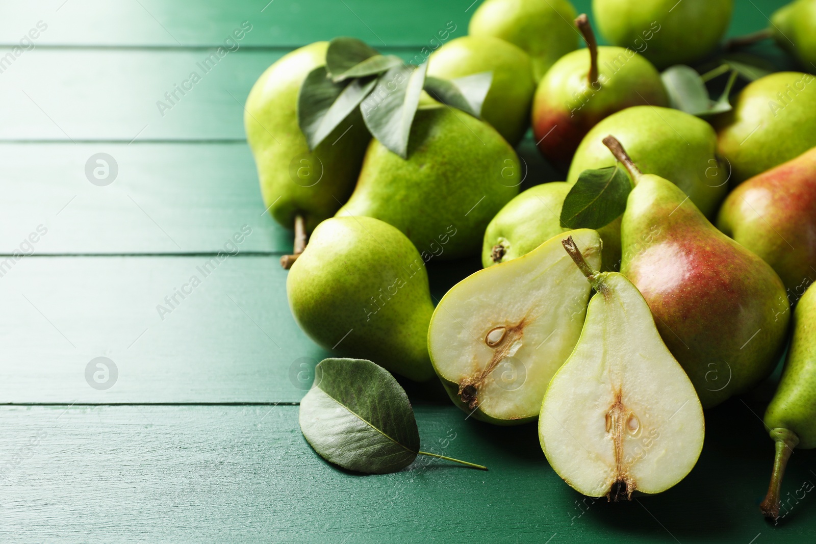 Photo of Fresh ripe pears and leaves on green wooden table, closeup. Space for text