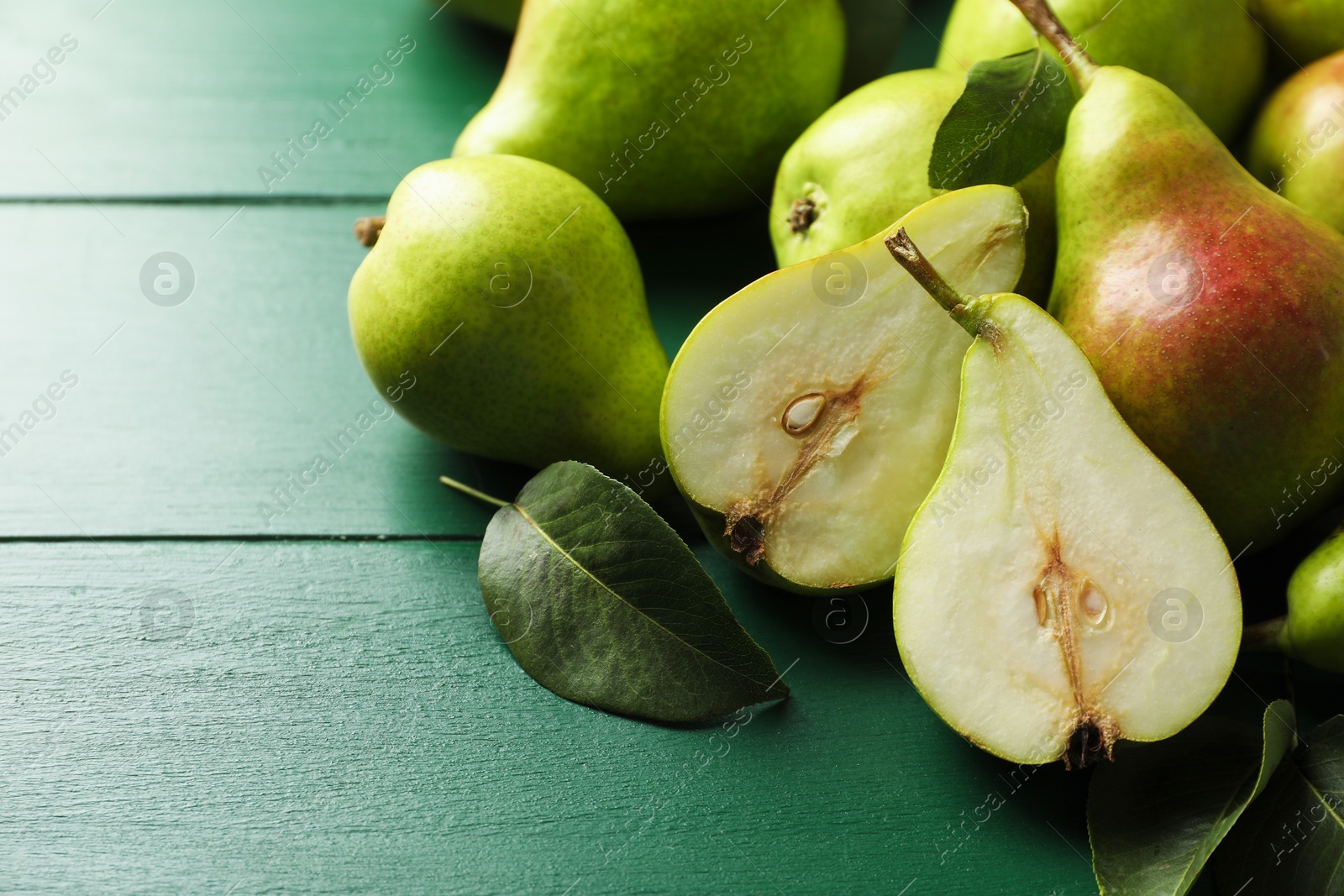 Photo of Fresh ripe pears and leaves on green wooden table, closeup. Space for text